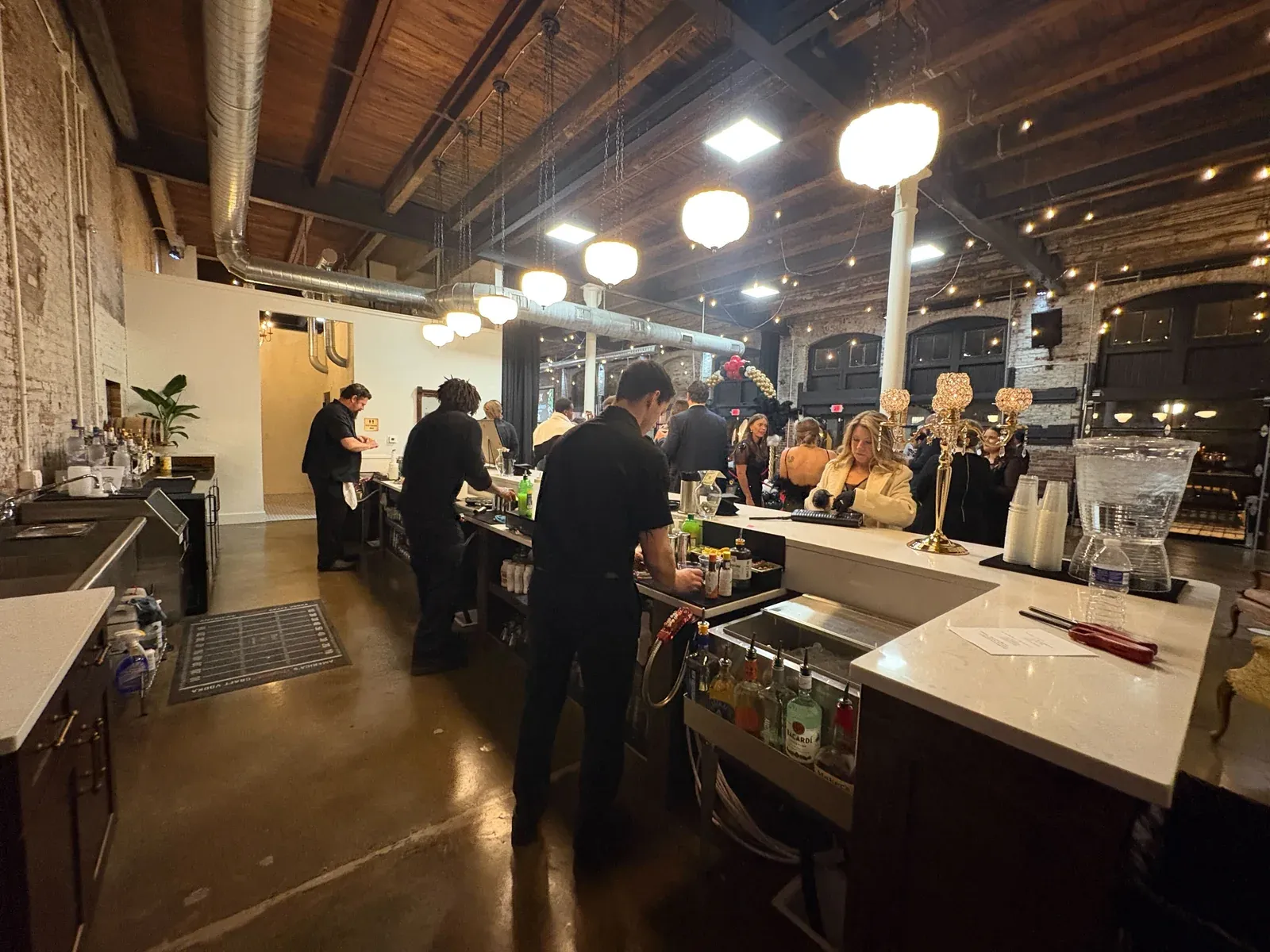Bartenders working the fully stocked bar in the Libations Lounge during an event at 24 Shelby, a downtown Indianapolis party venue with exposed brick and string lights