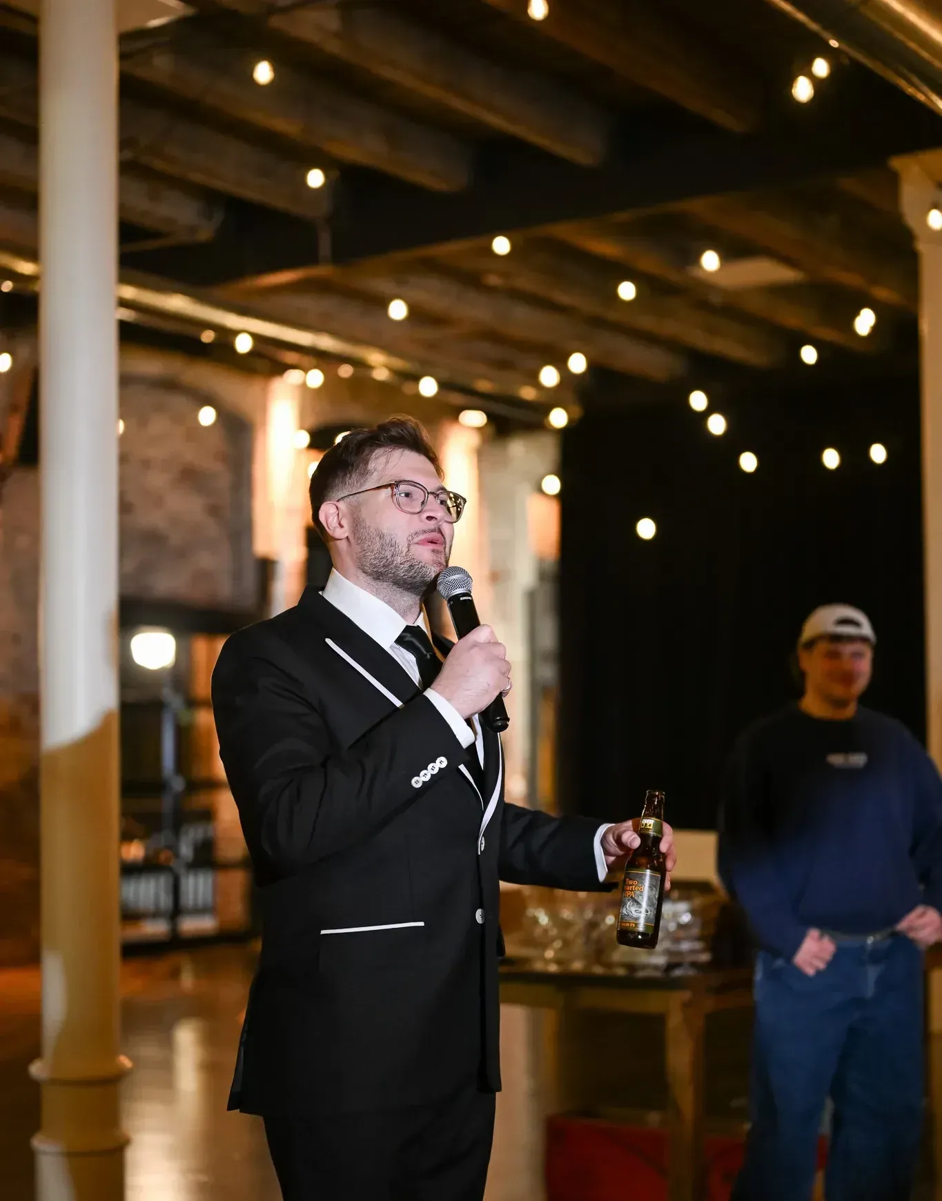 A speaker presenting at a corporate event venue in Indianapolis, 24 Shelby, using the in-house projection and raised stage under Edison lighting and exposed 1898 brick