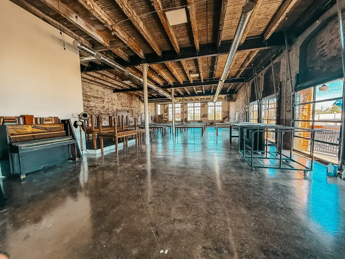 The Edison Room at 24 Shelby in its open setup, showing the original 1898 brick walls, exposed wood-beam ceilings, oversized windows, and Edison string lights: built-in venue character that decides whether a wedding venue is actually a value.