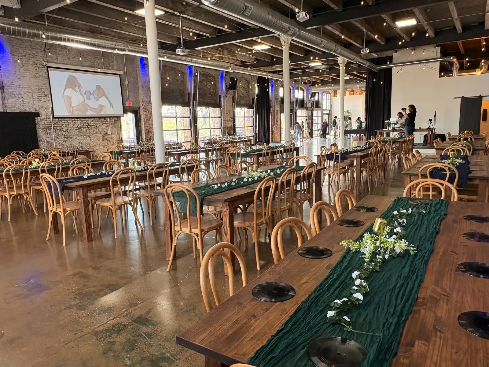 The main hall at 24 Shelby set with long farm tables and bentwood chairs for a graduation party in downtown Indianapolis, with a slideshow projected on the screen
