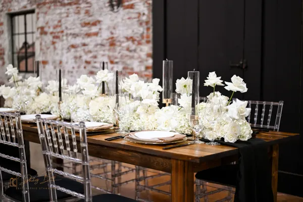 Long wooden reception table at 24 Shelby set with white florals, black taper candles, and ghost chairs against original 1898 exposed brick. The setup most Indianapolis couples picture when they imagine a downtown wedding.