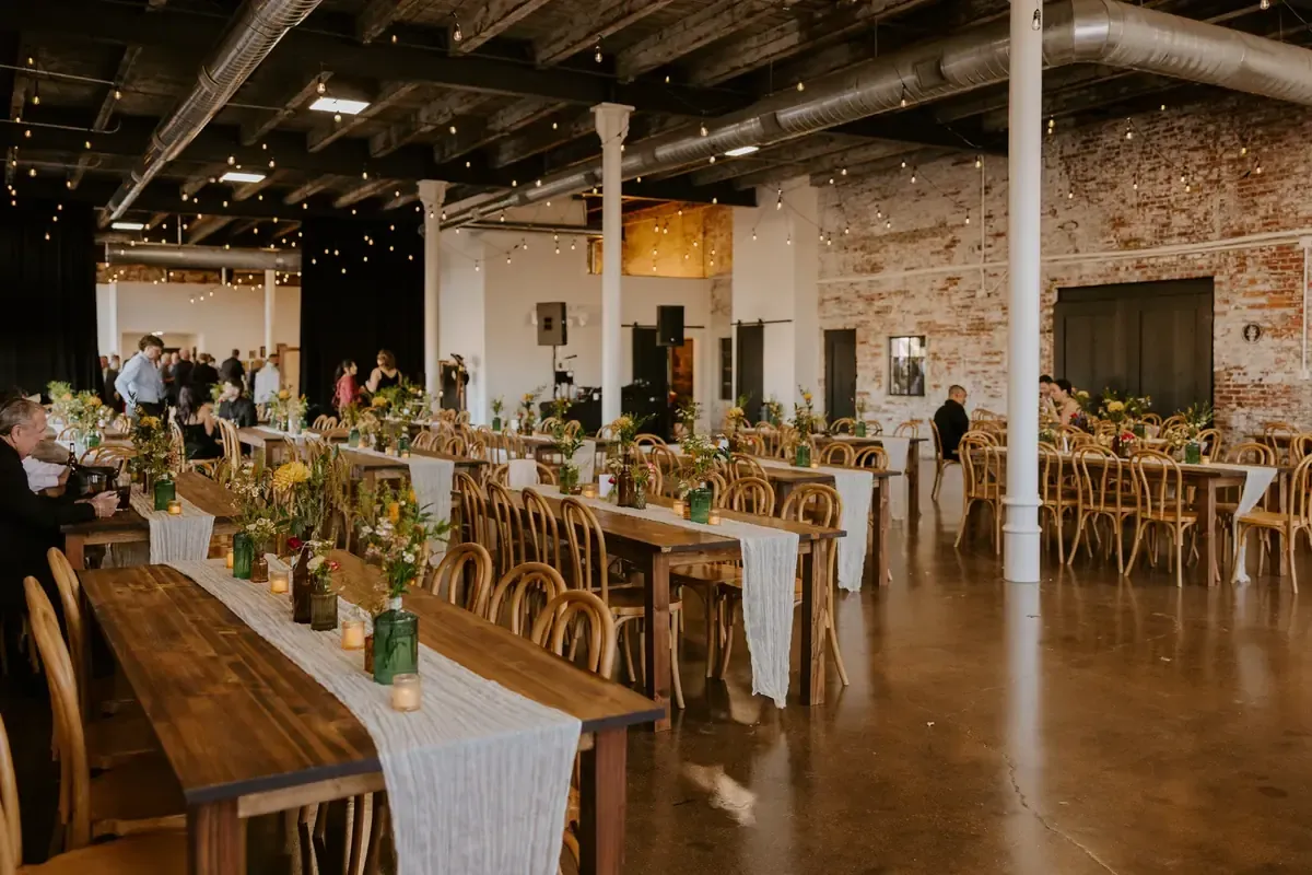 The Edison Room at 24 Shelby set for a Roaring Twenties wedding reception, with original 1898 exposed brick walls, oversized windows, and warm Edison string lights overhead, a historic 1920s wedding venue in downtown Indianapolis.