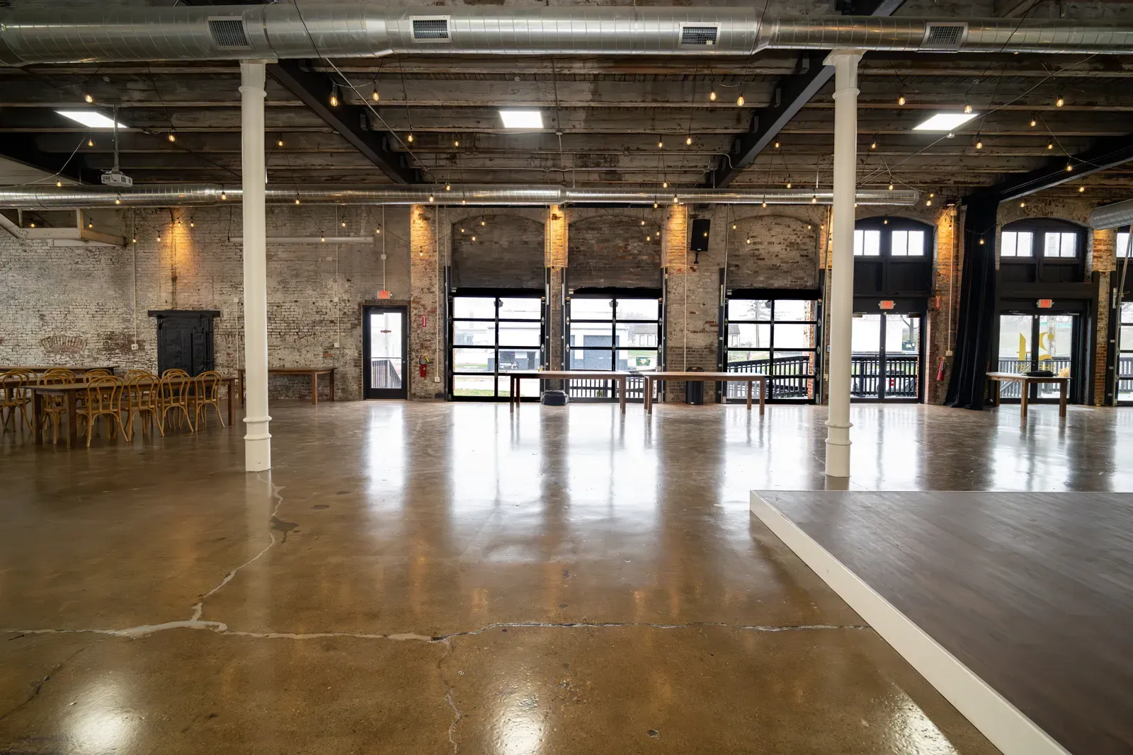 The open main hall at 24 Shelby with roll-up garage doors and polished concrete, the flexible floor an outside caterer stages service into at an Indianapolis wedding venue.